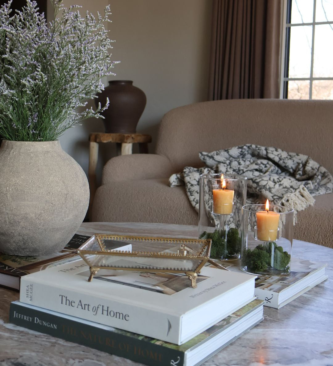 Styled marble coffee table with decorative items from the S. Flynn Home Store, such as a gray ceramic vase, a gold and glass tray, coffee table books, and locally made beeswax votive candles