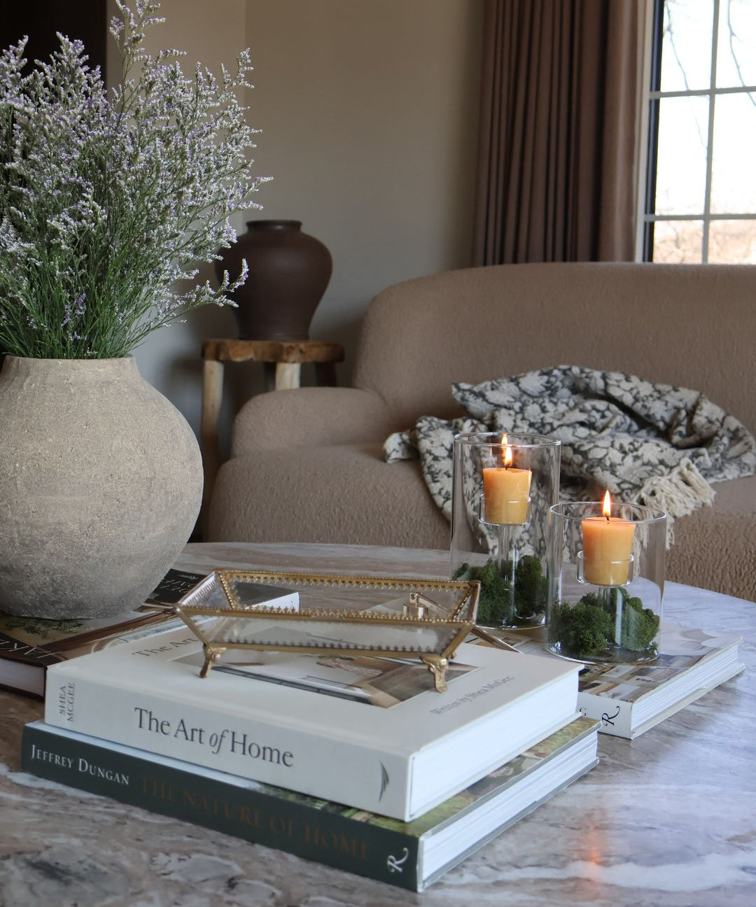 Styled marble coffee table with decorative items from the S. Flynn Home Store, such as a gray ceramic vase, a gold and glass tray, coffee table books, and locally made beeswax votive candles