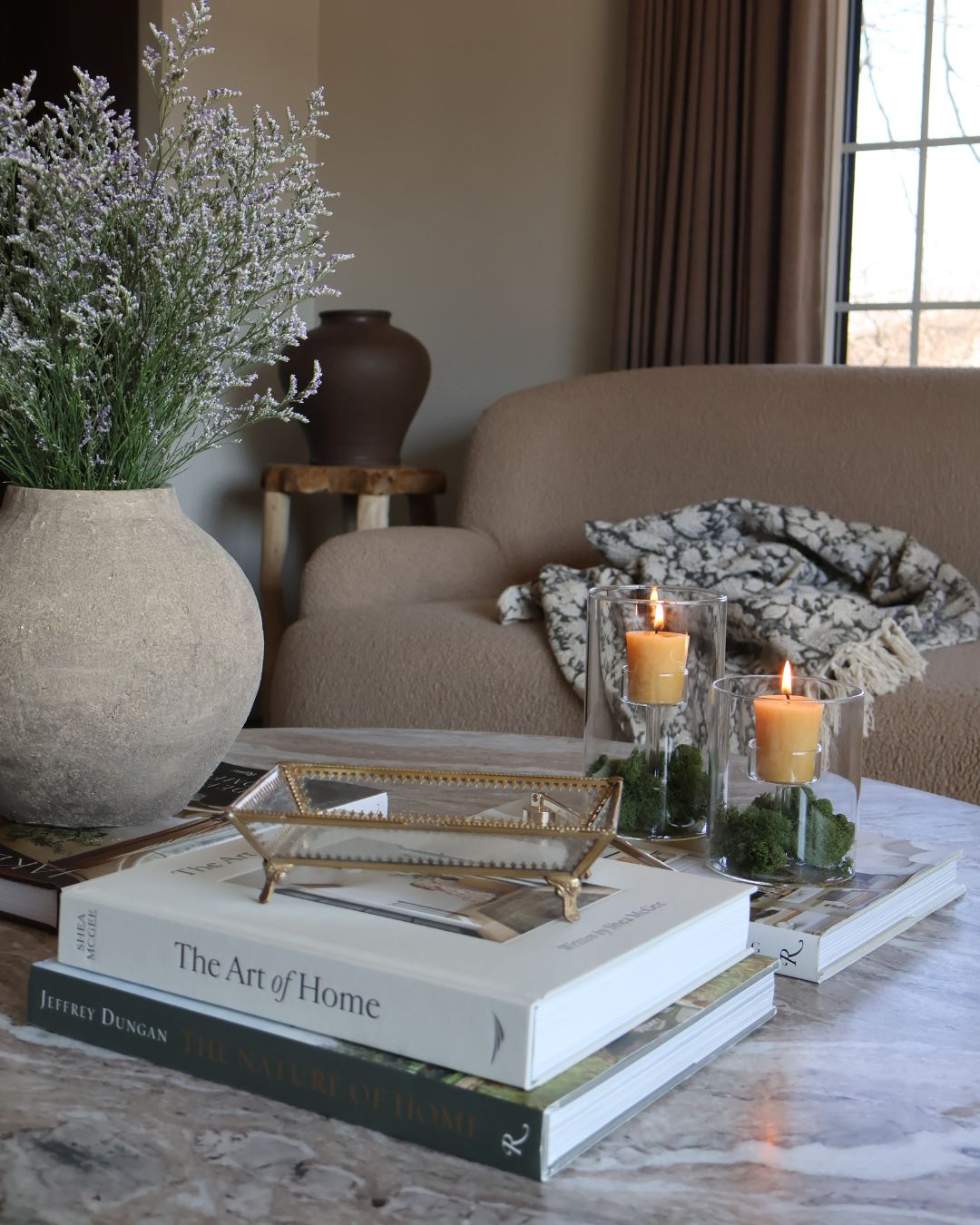 Styled marble coffee table with decorative items from the S. Flynn Home Store, such as a gray ceramic vase, a gold and glass tray, coffee table books, and locally made beeswax votive candles
