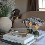 Styled marble coffee table with decorative items from the S. Flynn Home Store, such as a gray ceramic vase, a gold and glass tray, coffee table books, and locally made beeswax votive candles