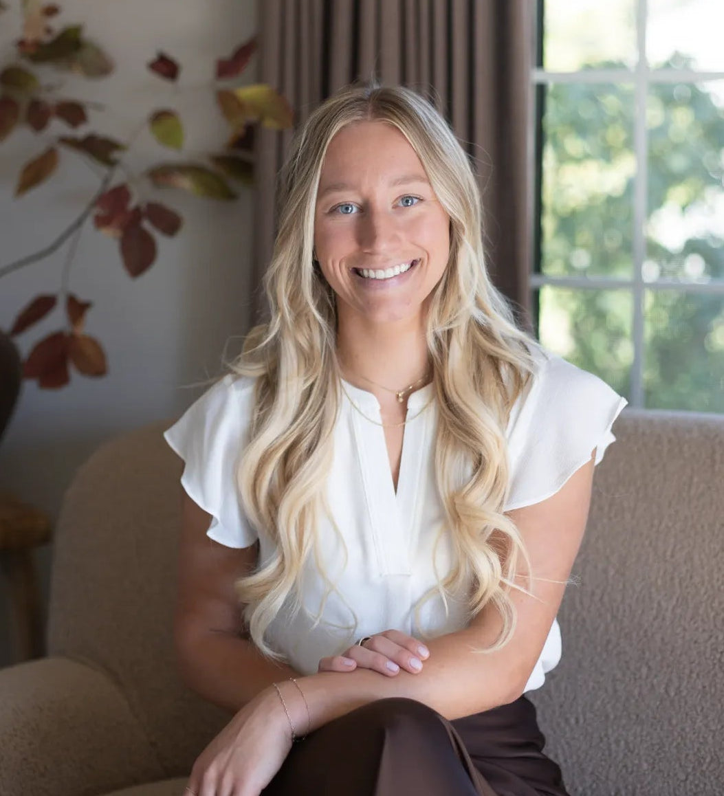 Marketing Manager sitting on a beige sofa in the S.Flynn Home Design + Build office with a bespoke vase behind her.