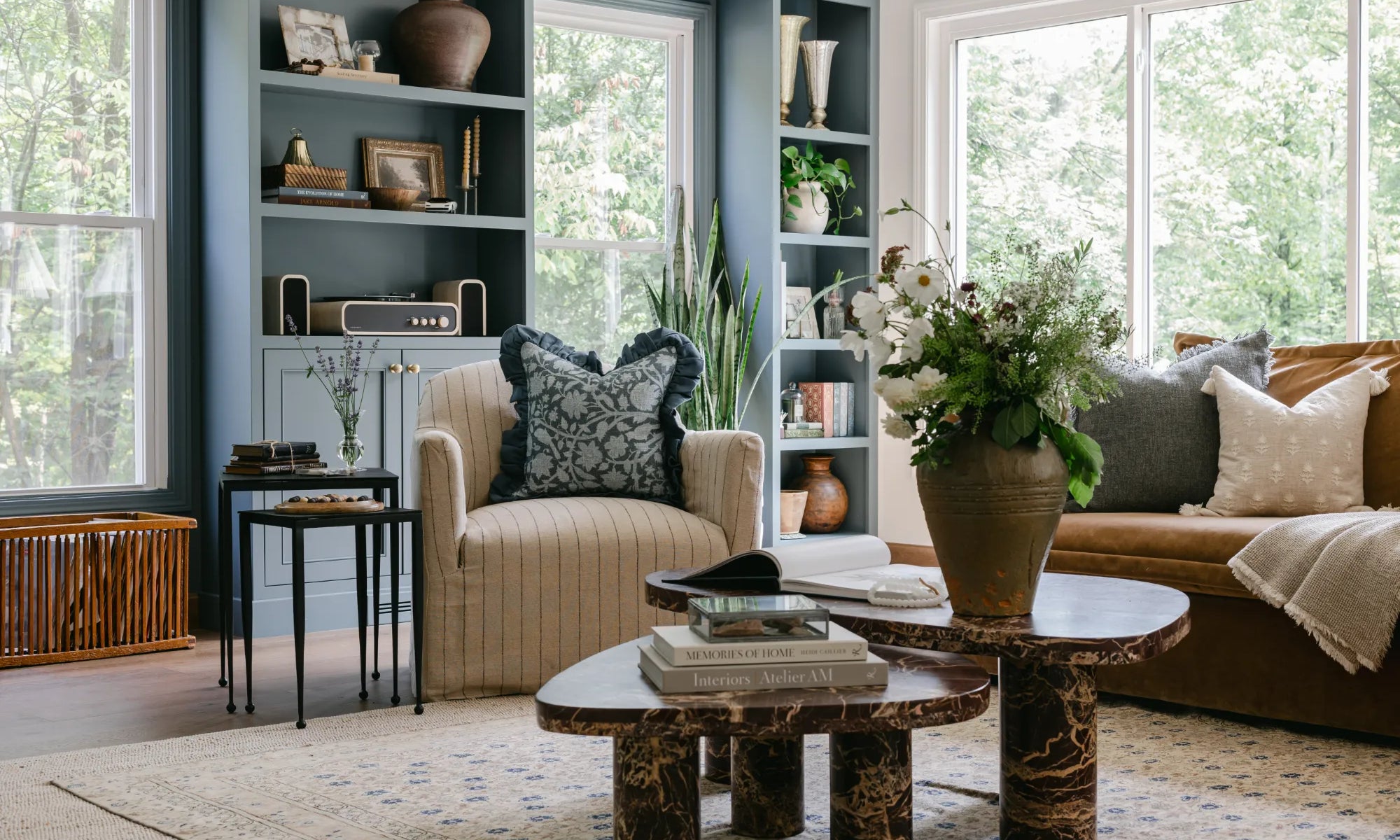 A beautifully designed living room showcasing S-Flynn home products such as a striped armchair, black side tables, marble coffee tables, coffee table books, textured vased, throw pillows and linen blankets.
