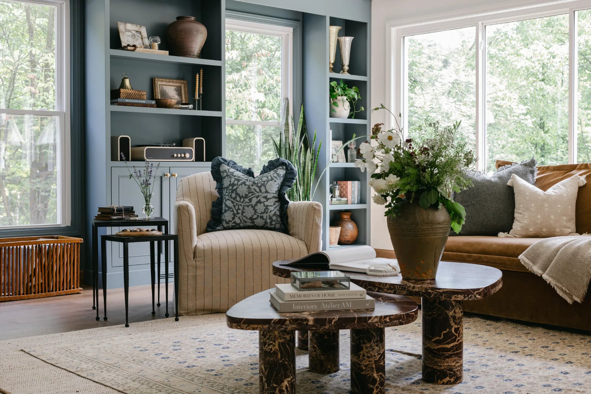 A beautifully designed living room showcasing S-Flynn home products such as a striped armchair, black side tables, marble coffee tables, coffee table books, textured vased, throw pillows and linen blankets.