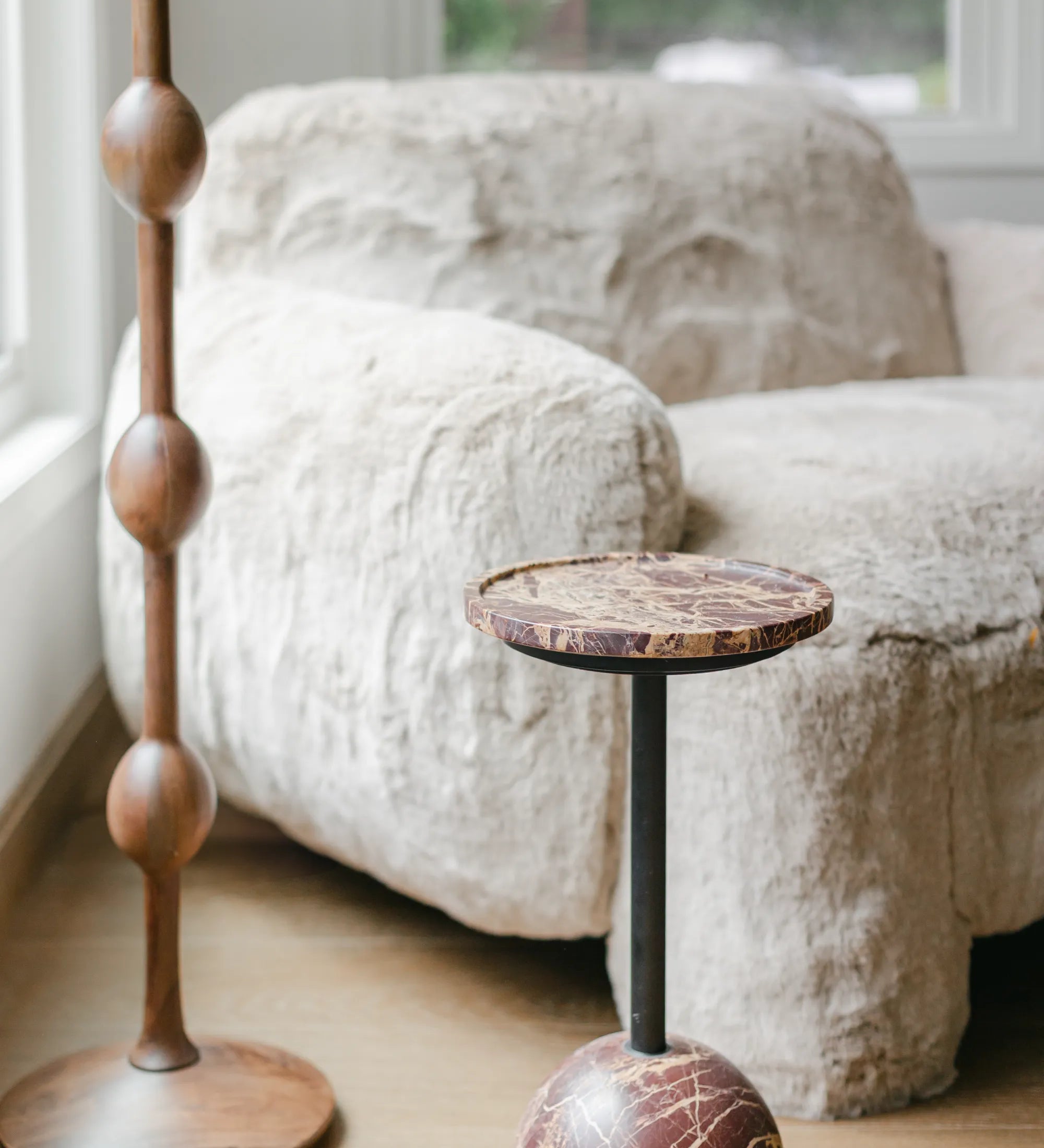 Decorative stools with wooden and marble bases in a room with a textured sofa and window, styled with S-Flynn Home products.