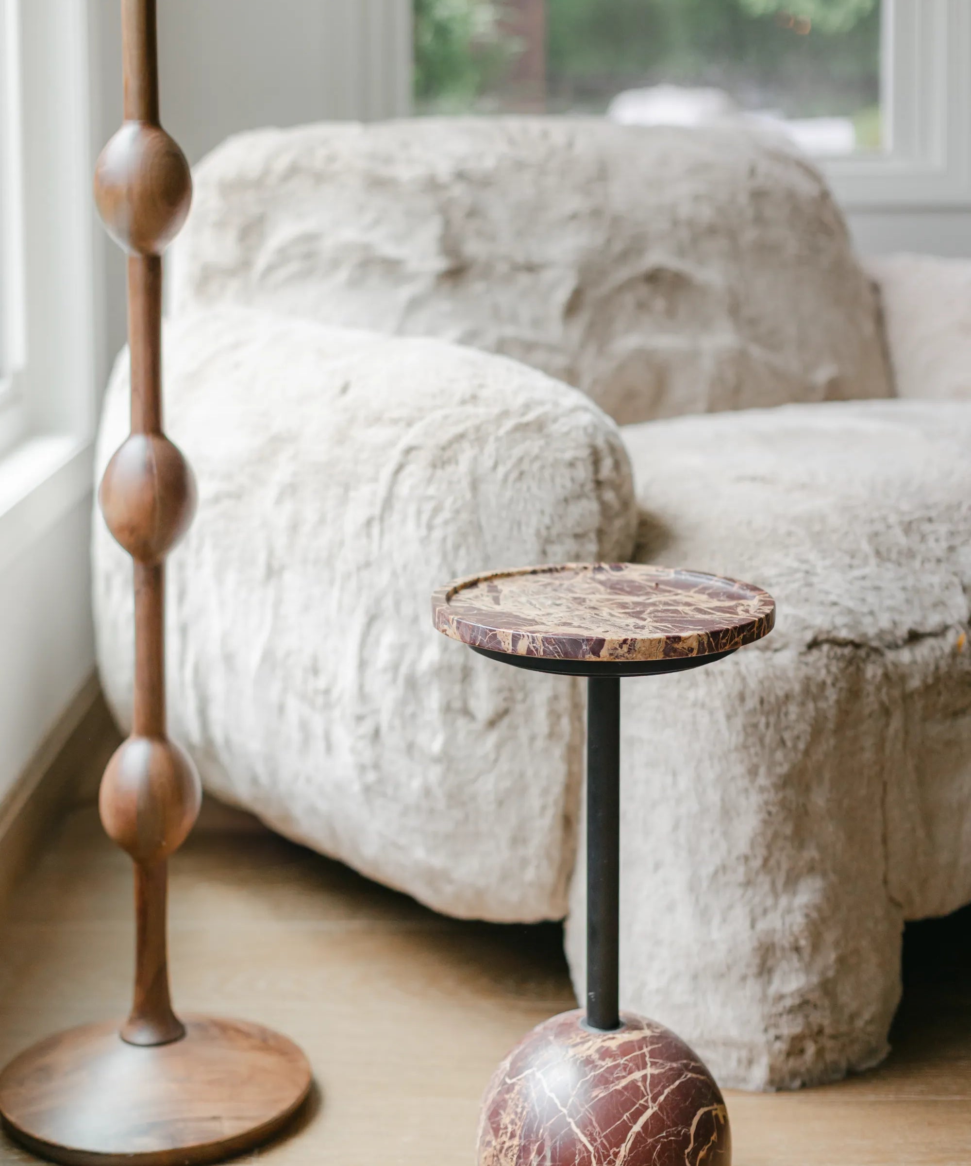 Decorative stools with wooden and marble bases in a room with a textured sofa and window, styled with S-Flynn Home products.